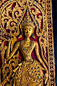 Wat Xieng Thong temple in Luang Prabang, Laos. Detail of a wooden door of the sim with gilded carvings on a red background. 